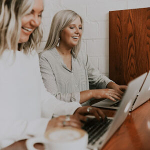 Two professionals women smiling while working on their laptops