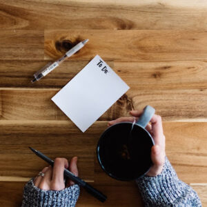 A woman holding a mug and a pen with a to-do list on a wooden table